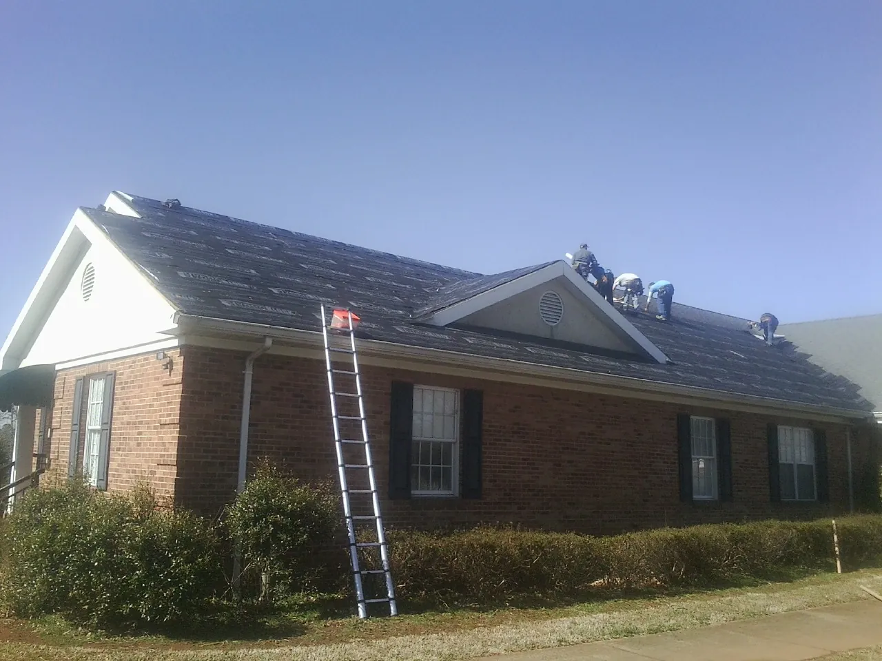 Crew tearing shingles off a brick ranch roof with a ladder set — Metal Roof Repair work by our crew in West Chesterfield
