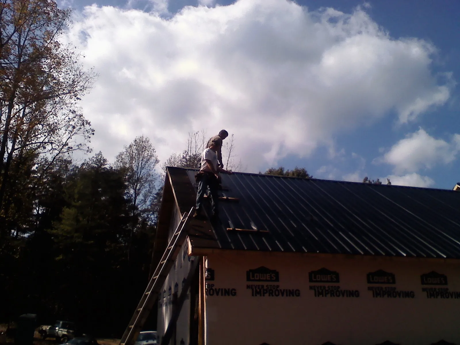 Roofer fastening dark metal panels high against a cloudy sky, from a Roof Inspection job in West Chesterfield