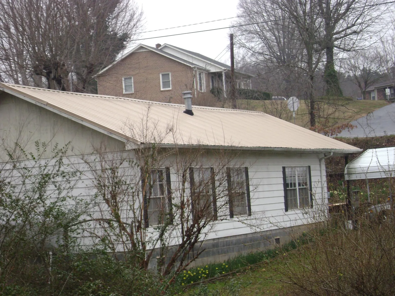 Tan metal roof on a white sided house set into a hillside — Commercial Roofing by Roofing Brothers in West Chesterfield